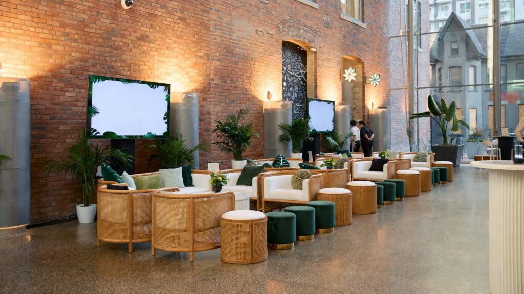 Corporate lounge: rattan armchairs and green ottomans grouped along a brick wall.
